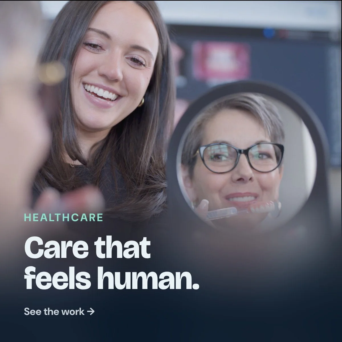 Healthcare: Care that feels human. A patient sees her new smile in a mirror as a team member smiles beside her.