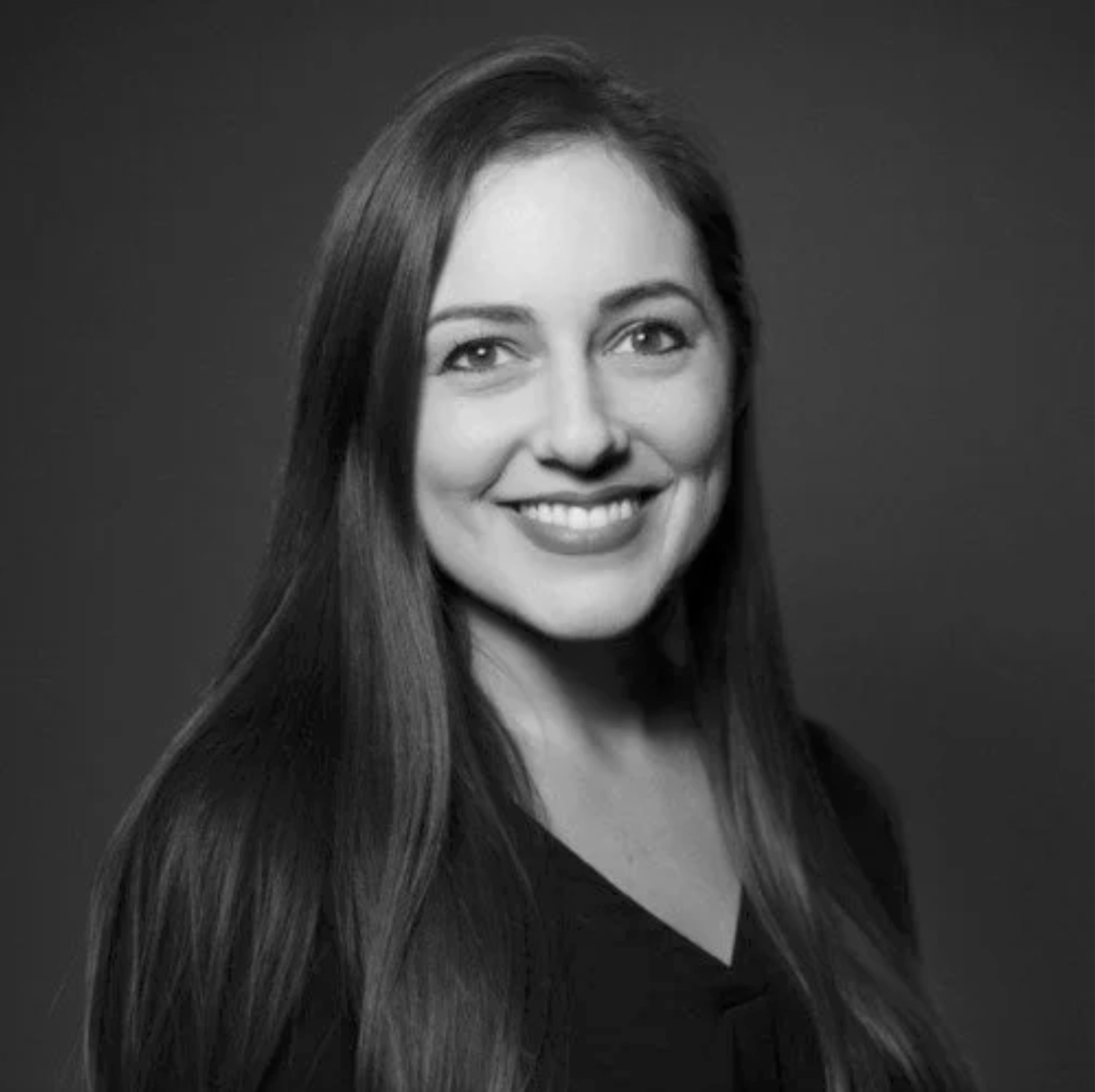 Black and white portrait of a smiling woman with long hair, wearing a dark top.