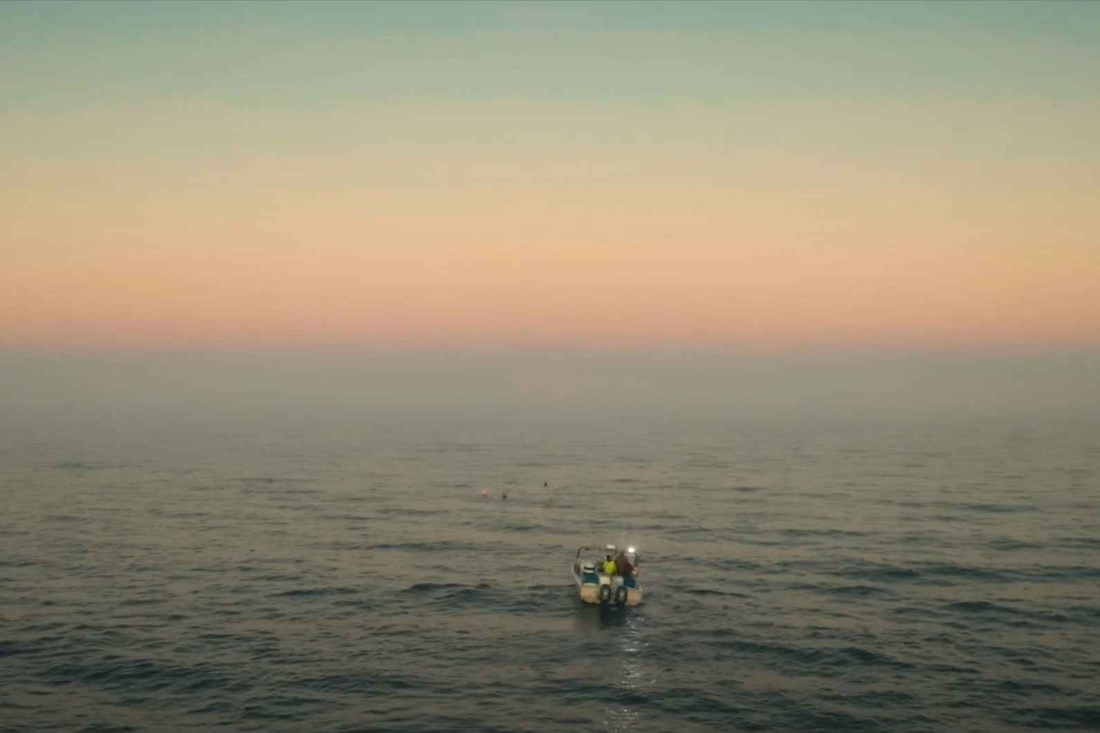 A boat with two people on it sailing in calm water at sunset, with a pastel-colored sky.