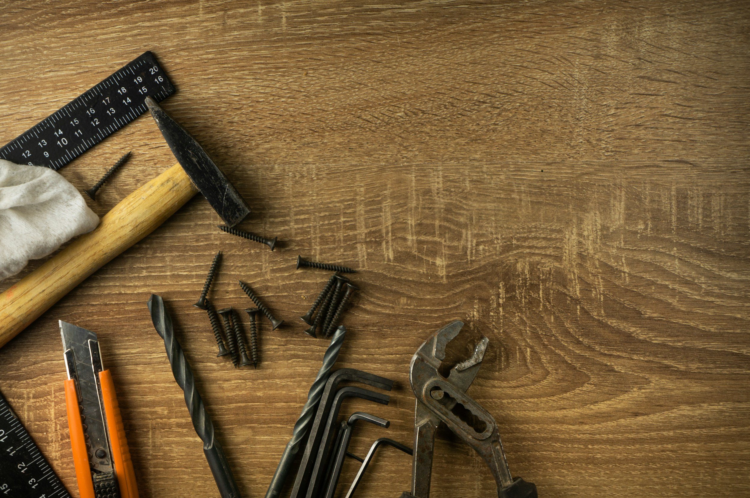 Een houten werkblad met diverse gereedschappen, waaronder een hamer, boormachines, schroevendraaiers, een verstelbare moersleutel, boortjes, schroeven en linialen.