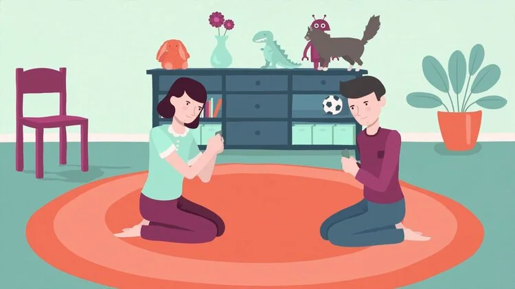 Two children sitting on a round orange rug indoors, playing with their phones. The room has a pink chair, a blue shelf with toys and books, and a potted plant. Decor includes a dog, dinosaur, and monster plush toys, with flowers in a vase on the shel