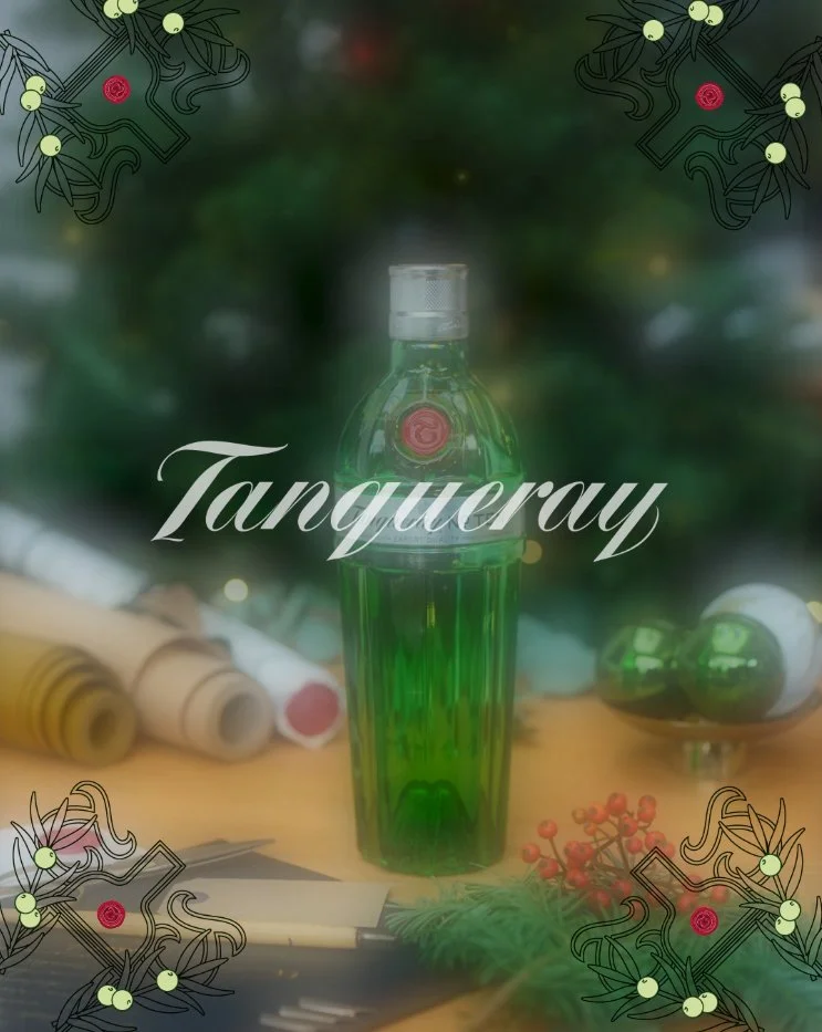 A green-tinted perfume bottle with a silver cap, labeled 'Tanqueray', surrounded by Christmas decorations and ornaments.