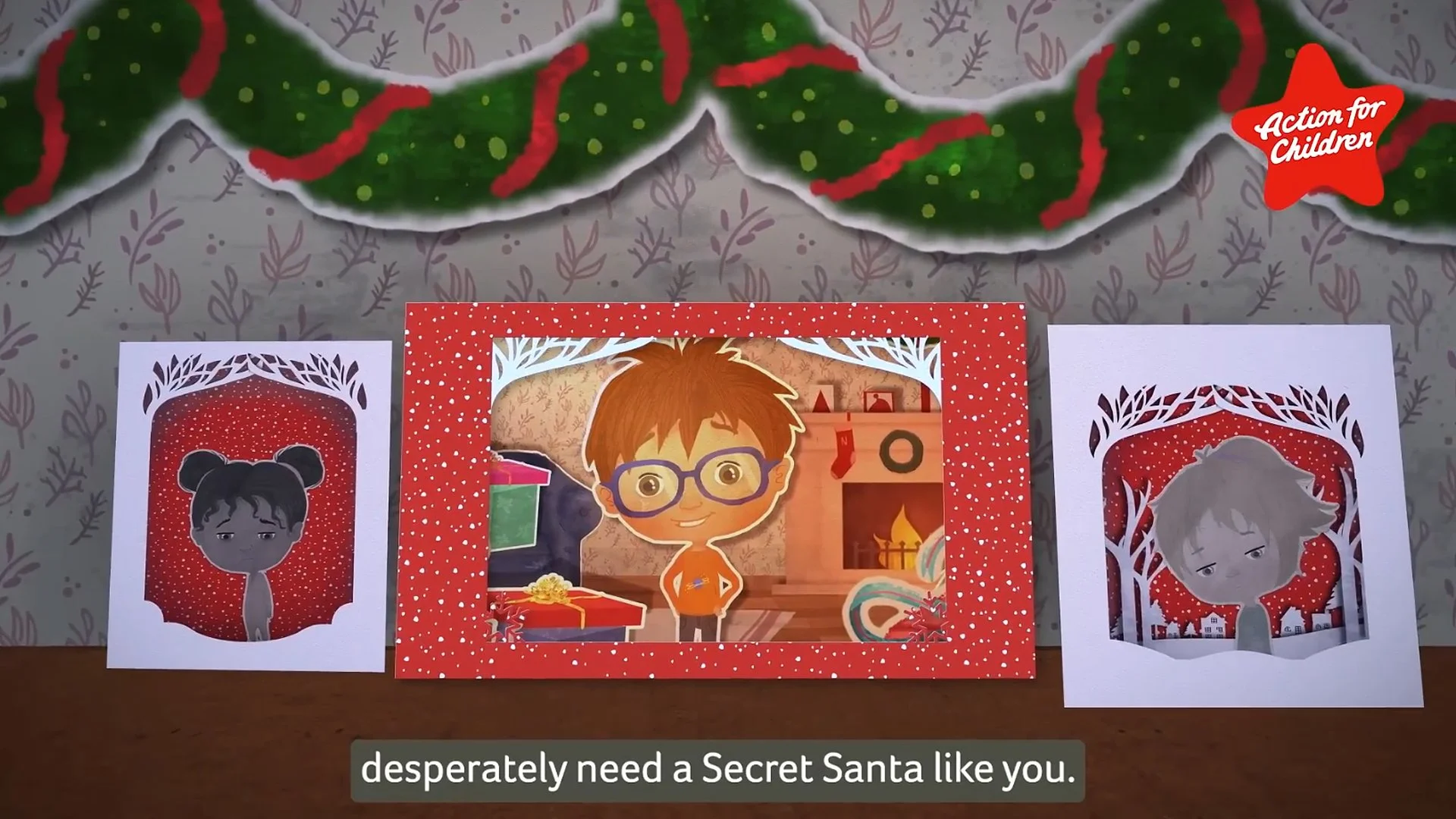 Three Christmas cards on a table with a garland hanging above. The center card features a cartoon boy with glasses in front of a fireplace, while the other two cards have illustrations of children in festive settings.