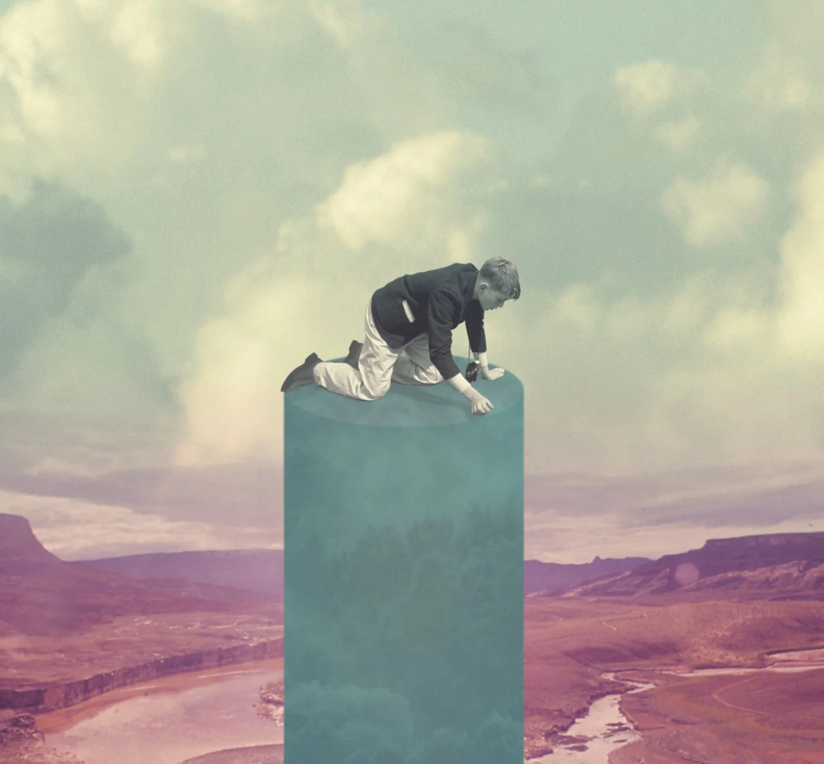 A person in formal attire crawling on top of a large teal rectangular block in a surreal landscape with distant mountains and a cloudy sky.