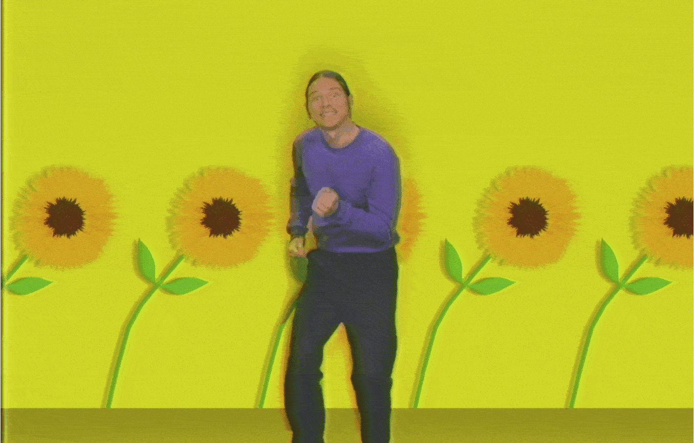 Person standing in front of a yellow wall with sunflower decorations, smiling and posing for the camera.