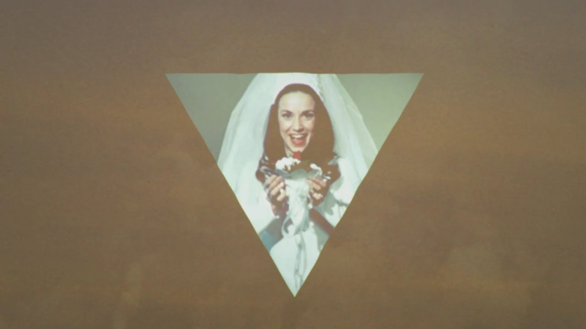 A projection of a woman dressed as a bride, holding a wedding bouquet, on a triangular surface.