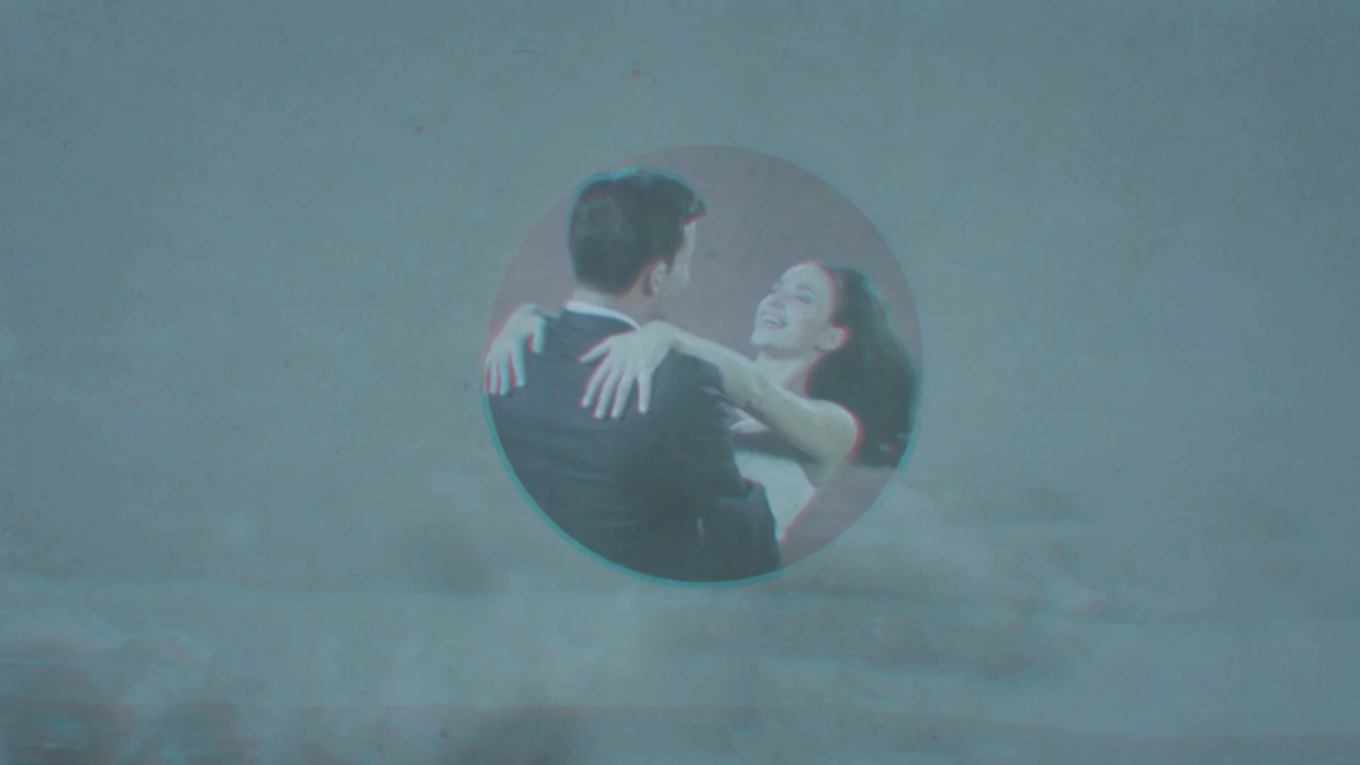 A man and woman dancing and smiling, seen through a circular reflective surface against a plain blue background.