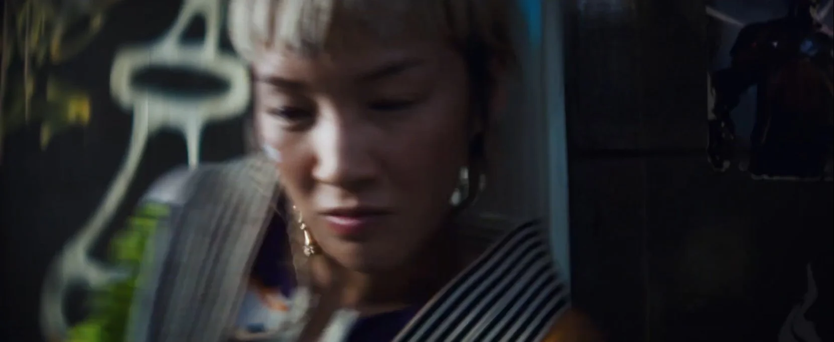 Close-up of a woman with short hair, wearing earrings and a striped shirt, looking down with a serious expression.