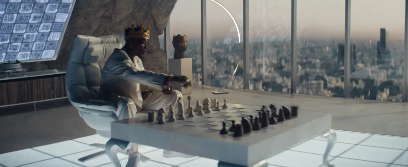 A person wearing a crown is sitting at a modern desk with a chessboard, in a high-rise office with a city view and large glass windows.
