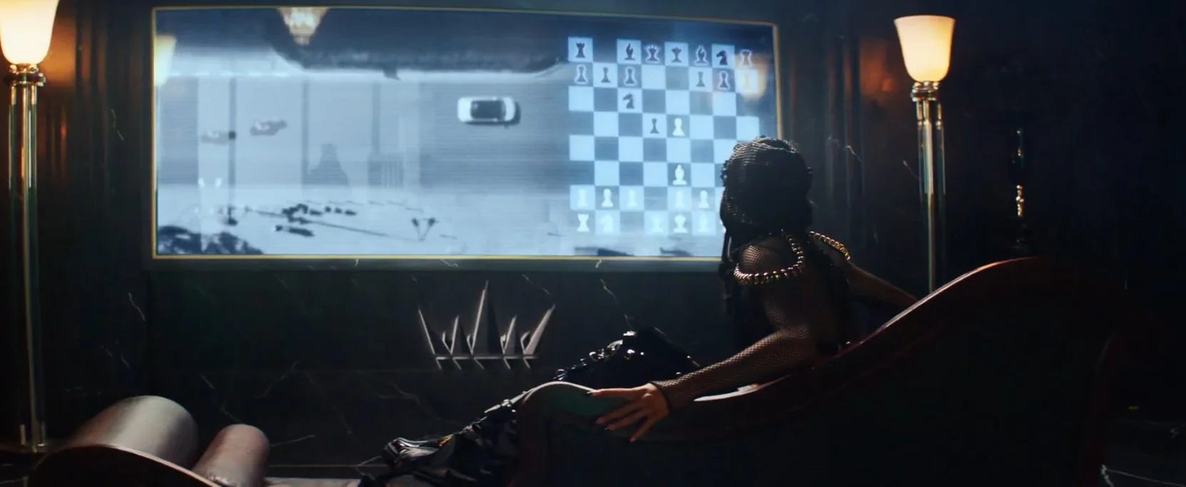 A woman with dark hair and fashion-forward clothing playing chess on a large screen, with a security camera view of a parking lot showing cars outside.