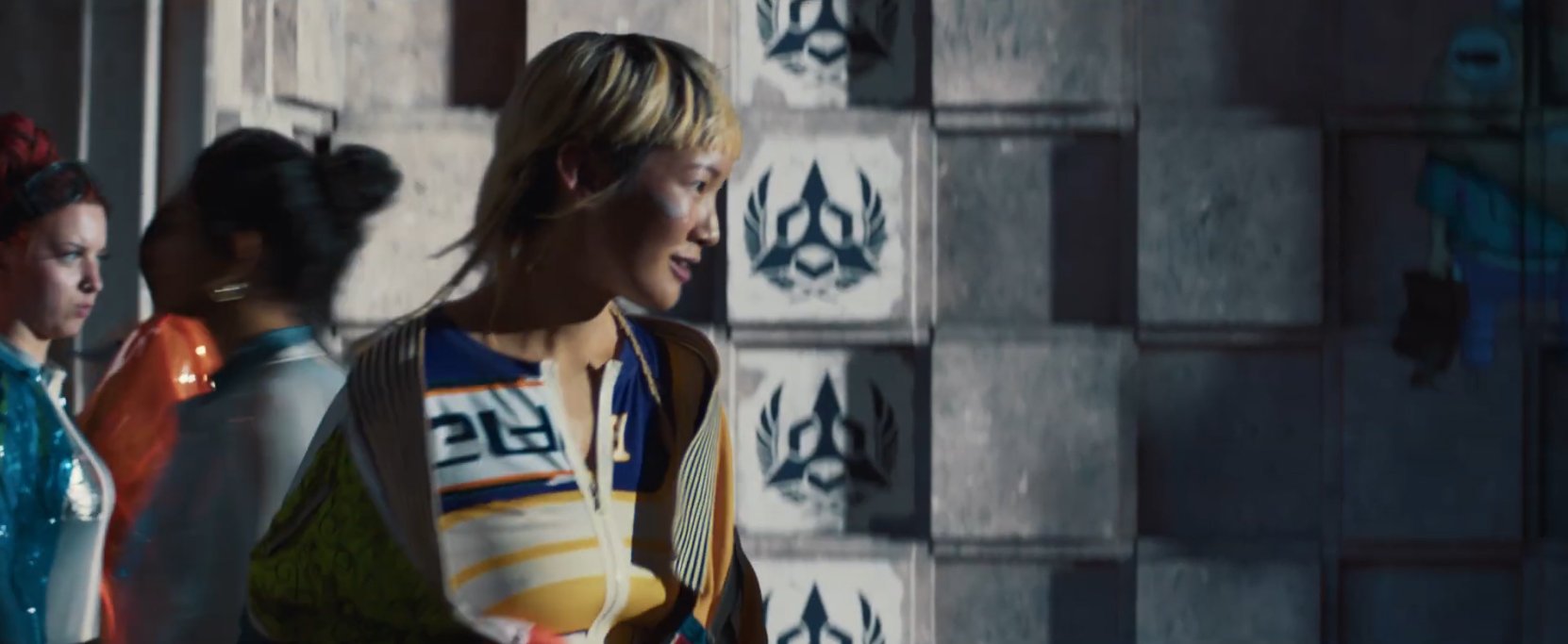 Three women walking in a modern, industrial-style interior with concrete walls and wall decorations featuring a lion head logo.