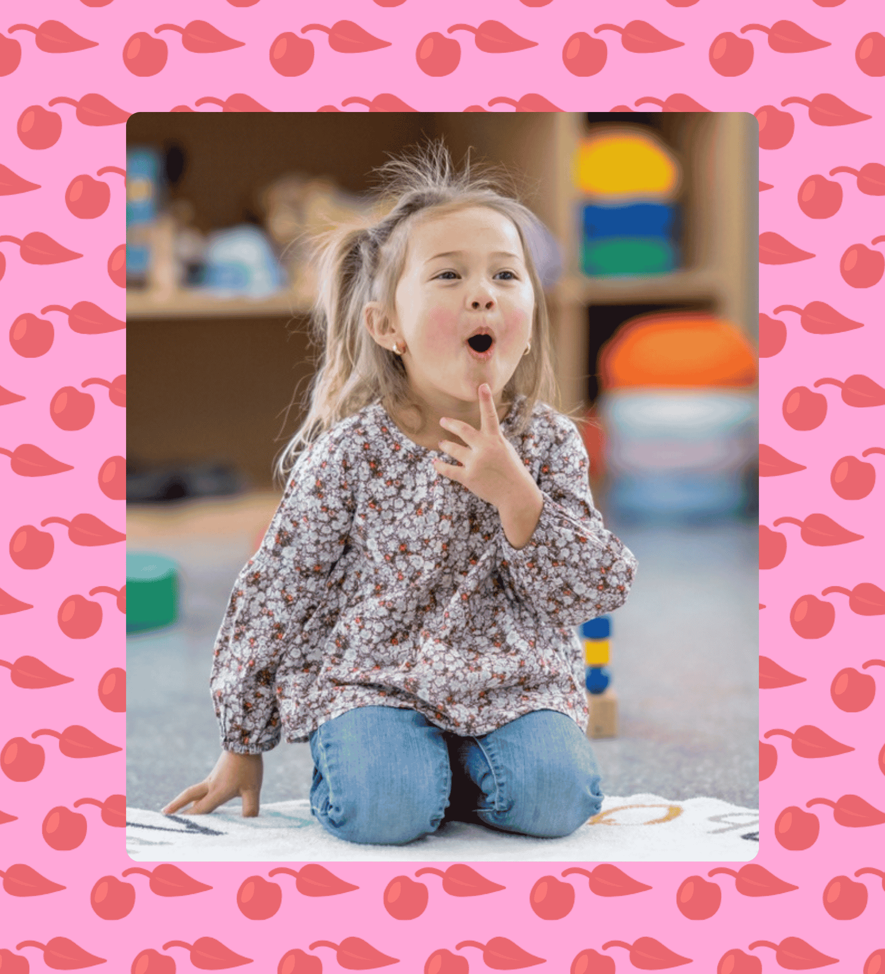 A young girl with blonde hair, wearing a floral-patterned long sleeve top and blue jeans, kneeling on a patterned rug while working on speech sounds during speech therapy for childhood apraxia of speech in Newport News, VA.