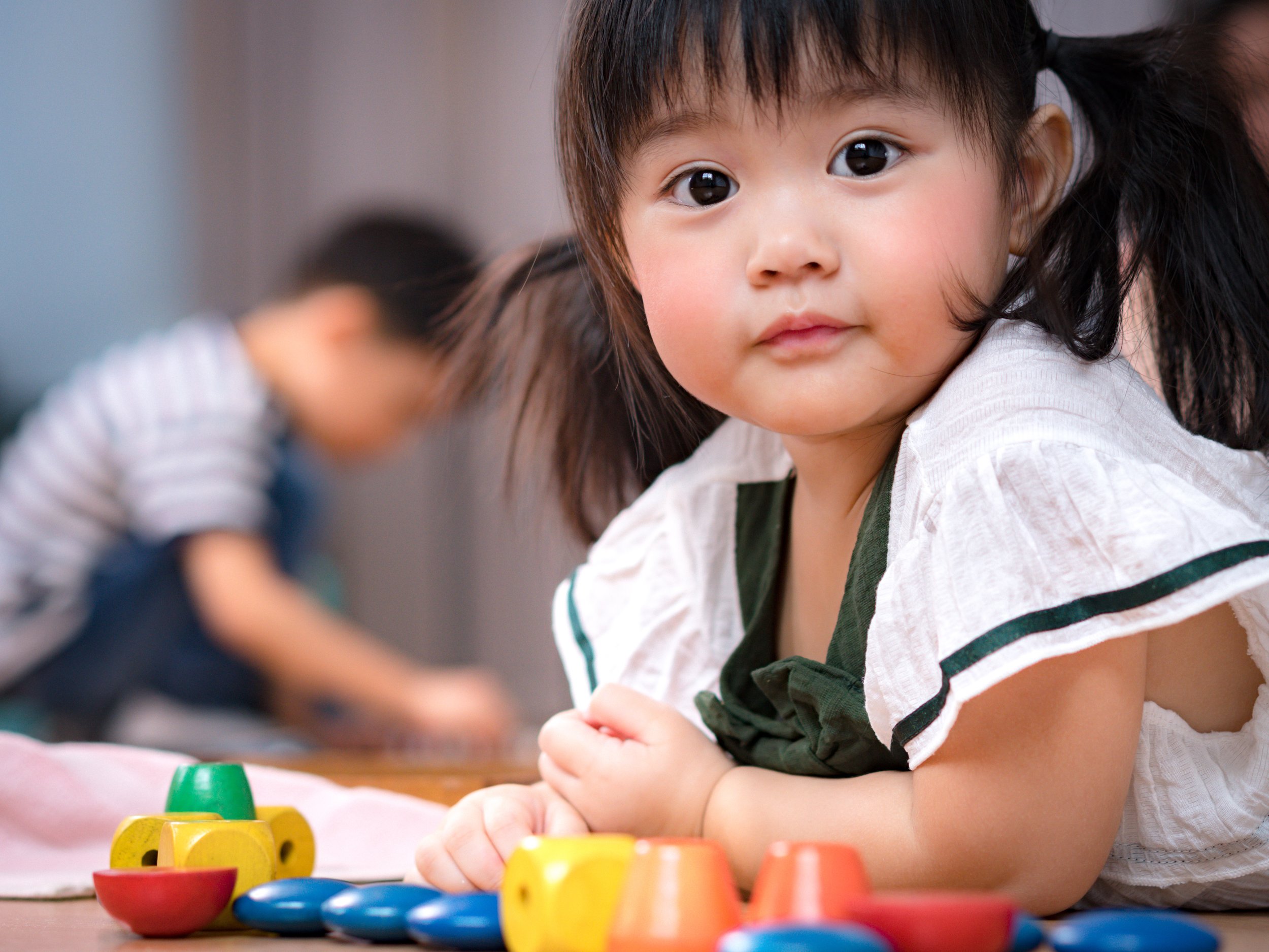 A young girl with dark hair styled in pigtails, sitting at a table with colorful blocks during speech therapy for late talkers in Newport News, VA.
