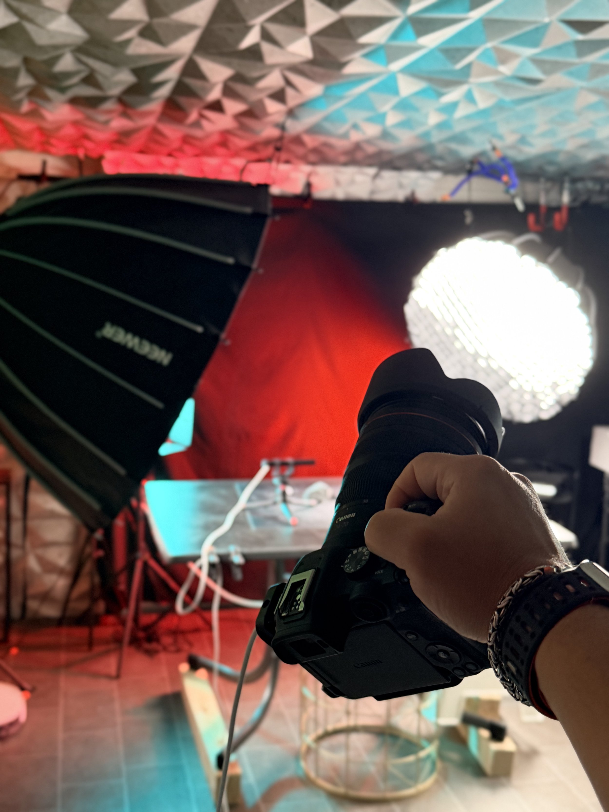 Eine Person hält eine Kamera in der Hand, während im Hintergrund eine leuchtende Lichtquelle aufgestellt ist. Der Raum ist mit einem bogenförmigen, isolierten Deckenabsorber und weiteren technischen Geräten ausgestattet.