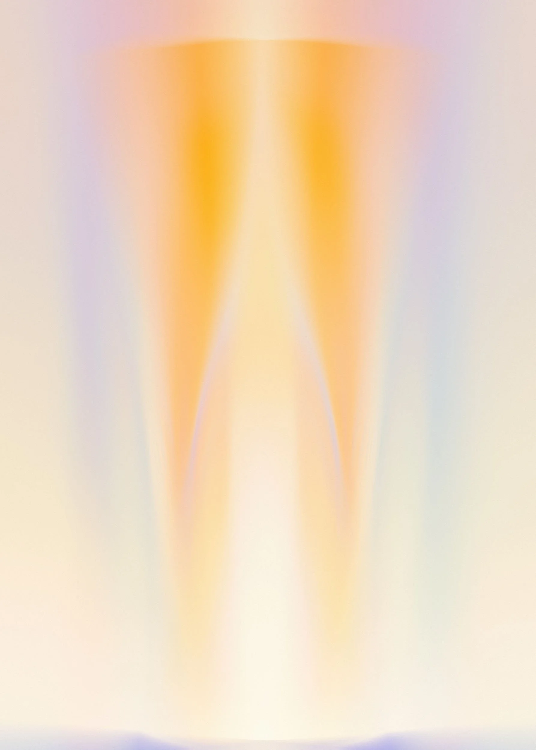Soft focus image of a tall glass filled with an orange-yellow liquid, possibly juice or a beverage, on a plain surface with a neutral background.
