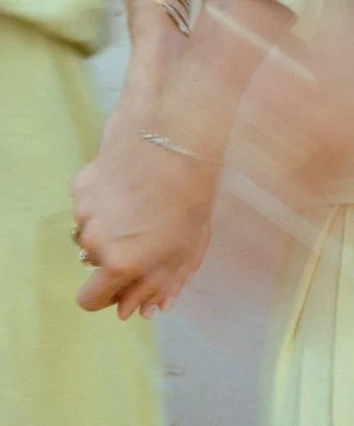Close-up of two people holding hands, one wearing a gold ring on the ring finger.