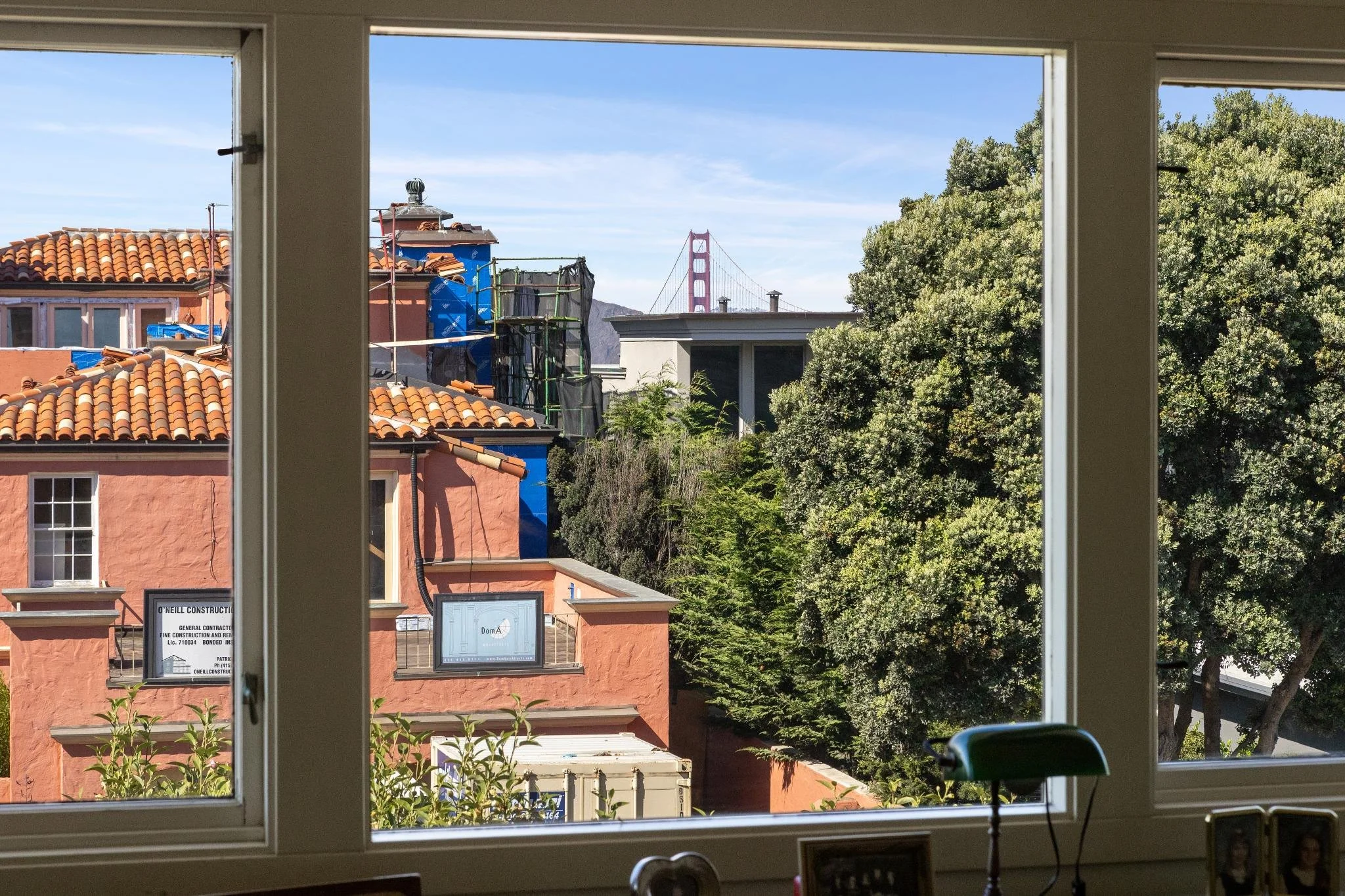 View of San Francisco Bay, including the Golden Gate Bridge, through a window with buildings, trees, and a blue sky in the background.
