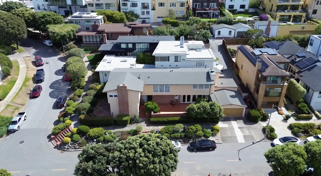 Aerial view of 201 Sea Cliff Avenue, and the Sea Cliff neighborhood, San Francisco with multiple houses, trees, and parked cars along the streets.