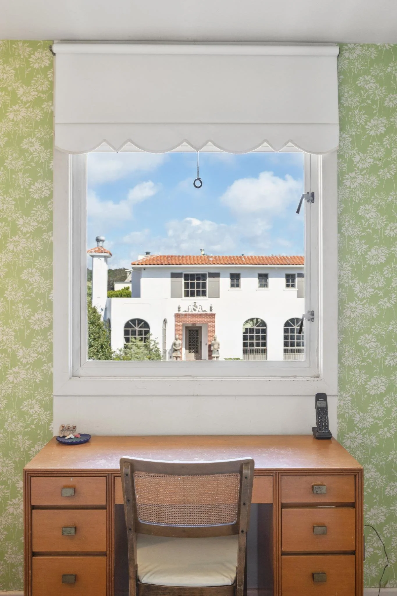 View from a window showing a white building with a red-tiled roof and blue sky with clouds.