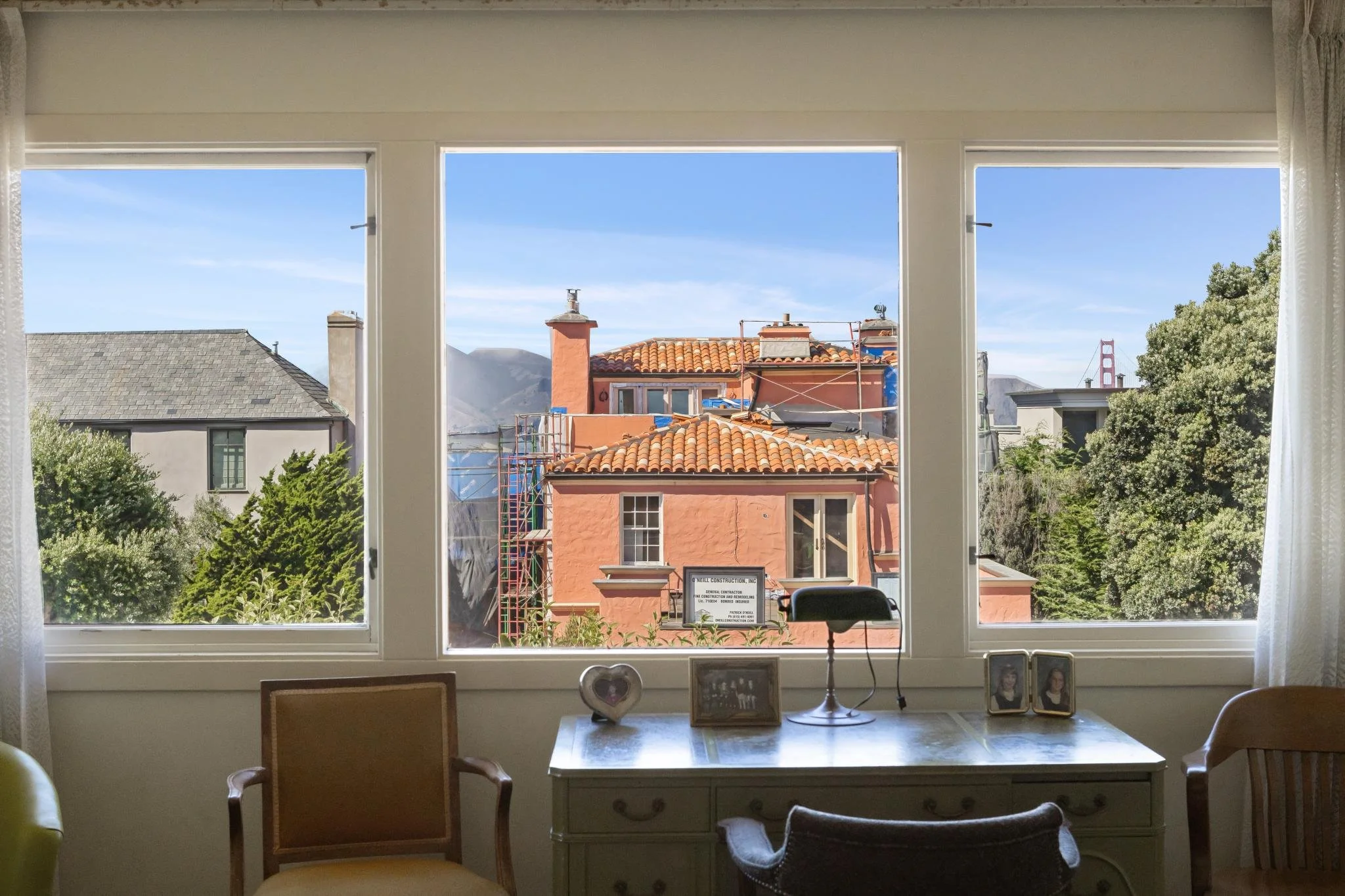 View of rooftops and chimneys through a large window in a home, with clear blue sky in the background.