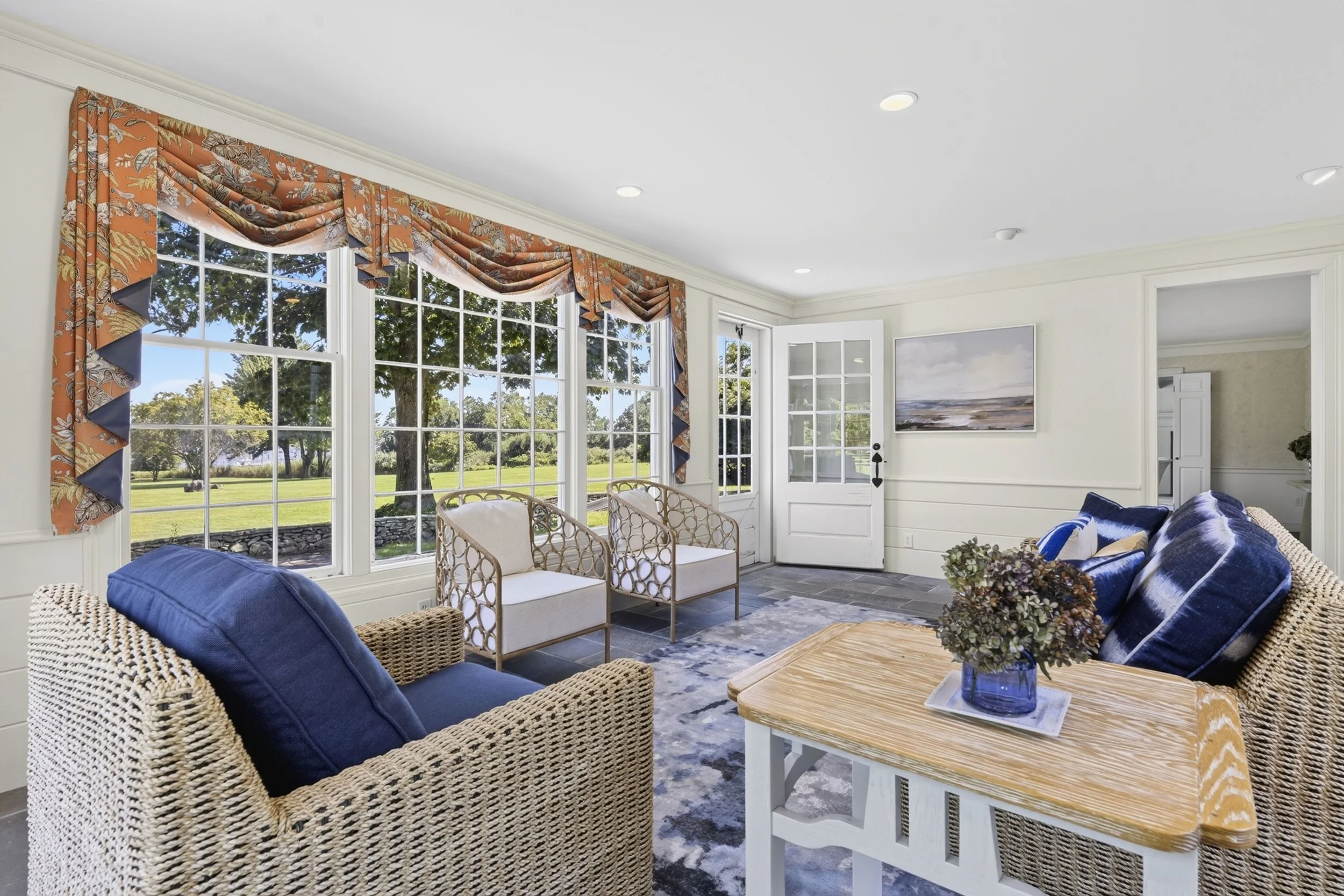 Living room with large windows, floral curtains, wicker and upholstered furniture, and ocean view