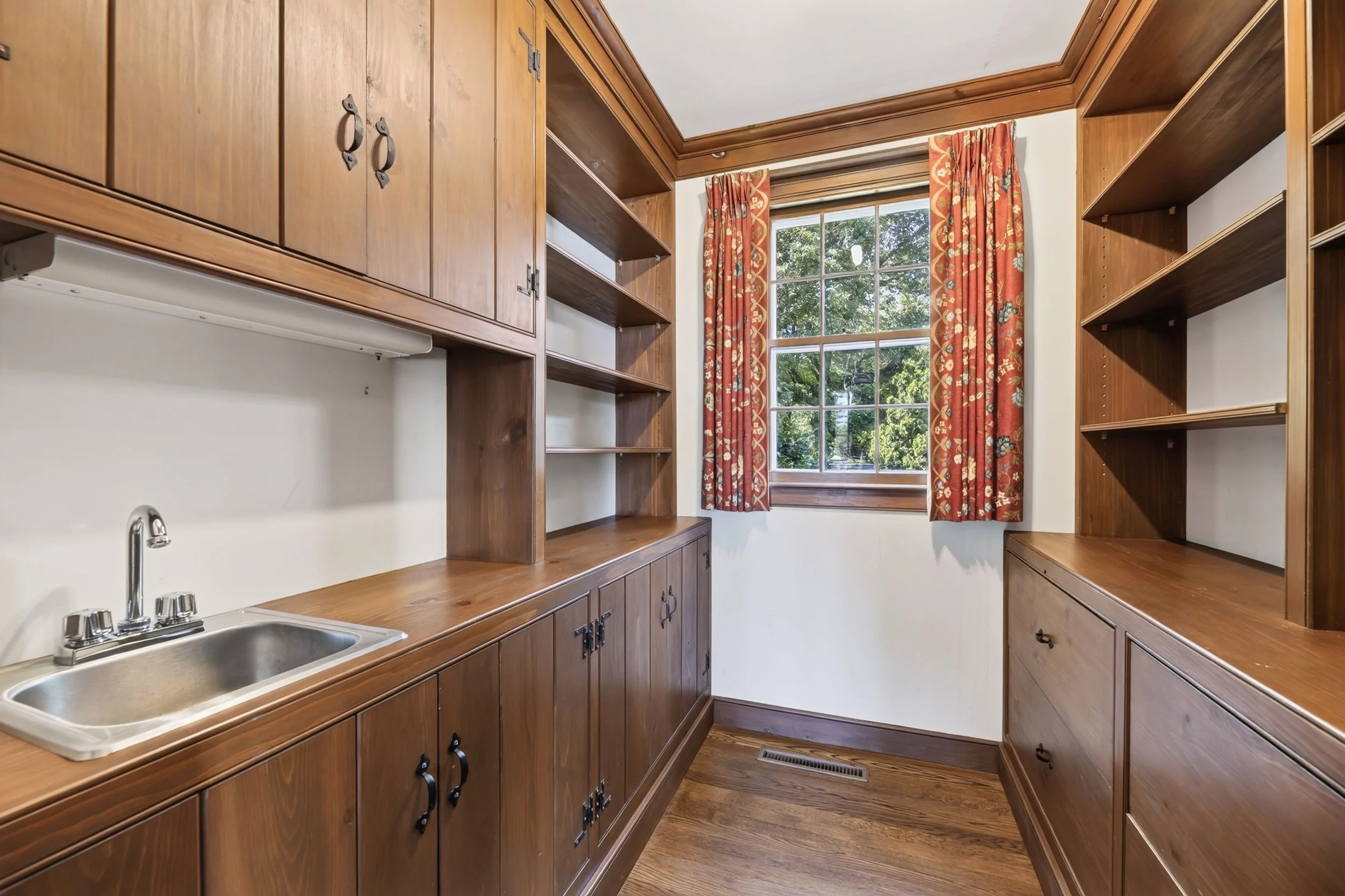 Kitchen with wooden cabinets, a window with red patterned curtains, and a stainless steel sink.