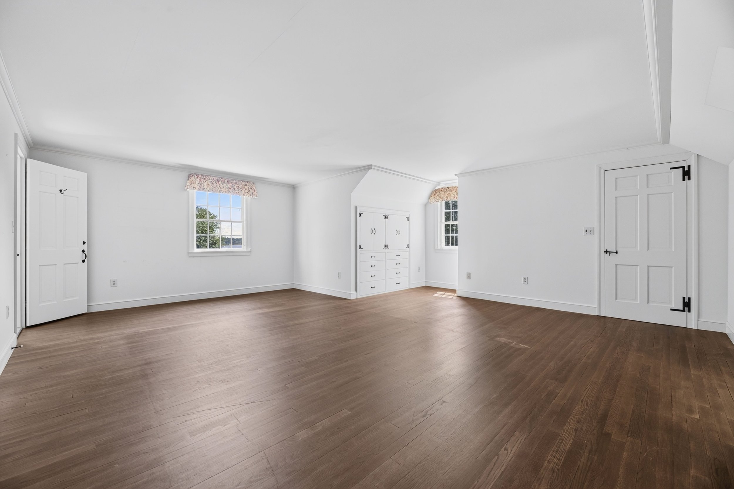 Empty white room with two windows, white doors, and hardwood flooring.