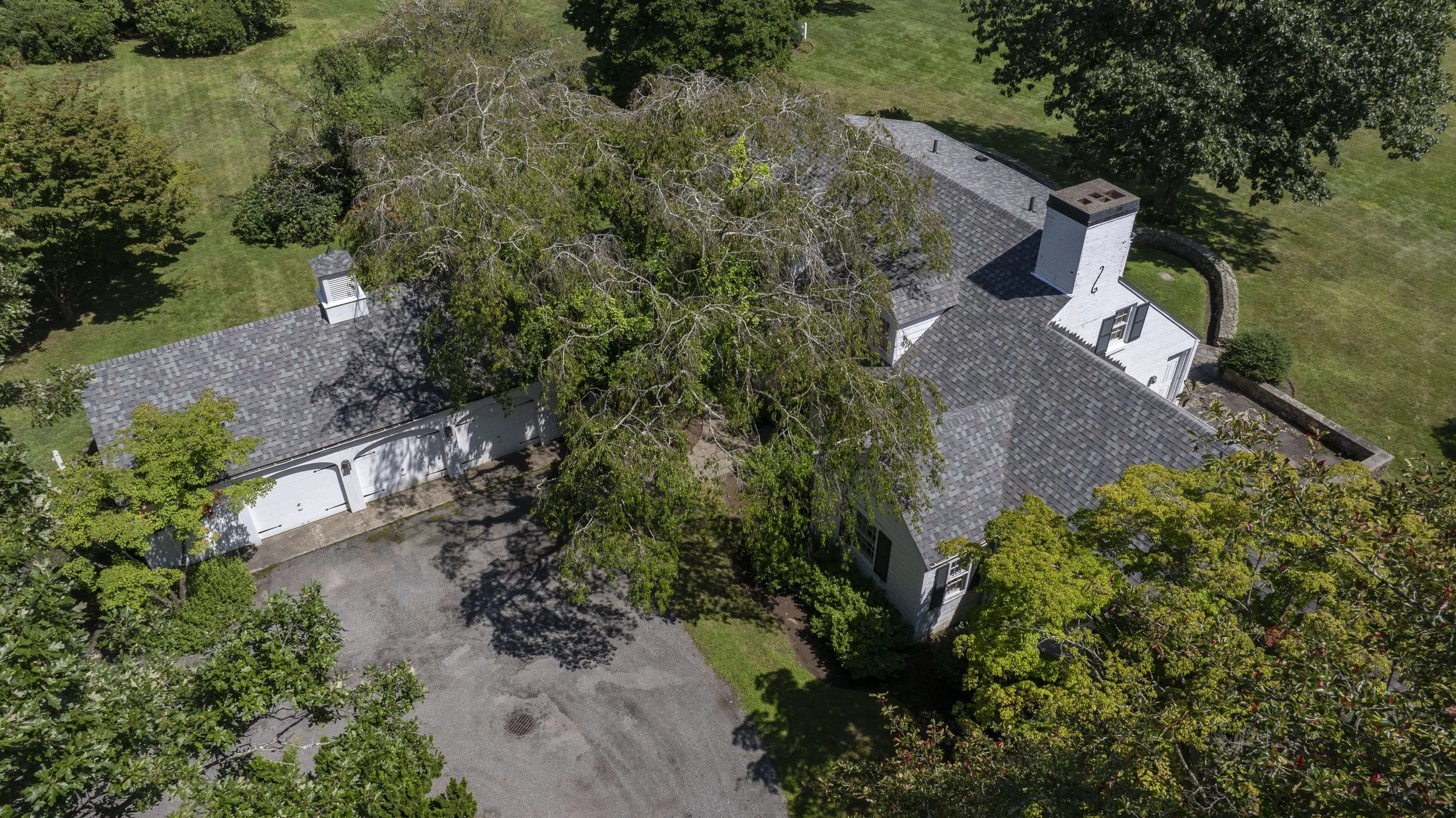 An aerial view of a house with a slate roof surrounded by trees and green lawns.