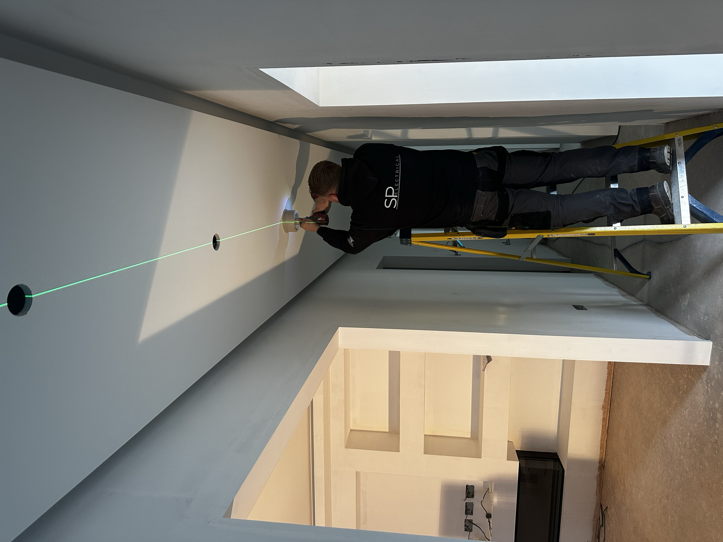     SP Electrical electrician installing ceiling lighting using laser guided alignment.