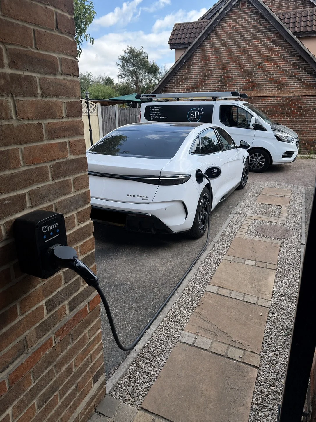 Ohme home EV charger connected to a white electric car outside a property.