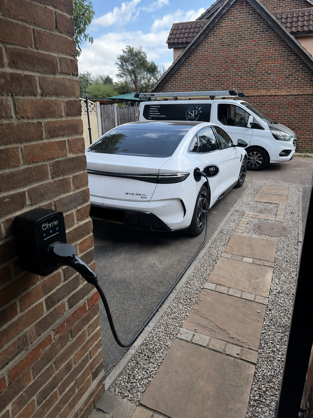     Ohme EV charger connected to a white electric car on a residential driveway.