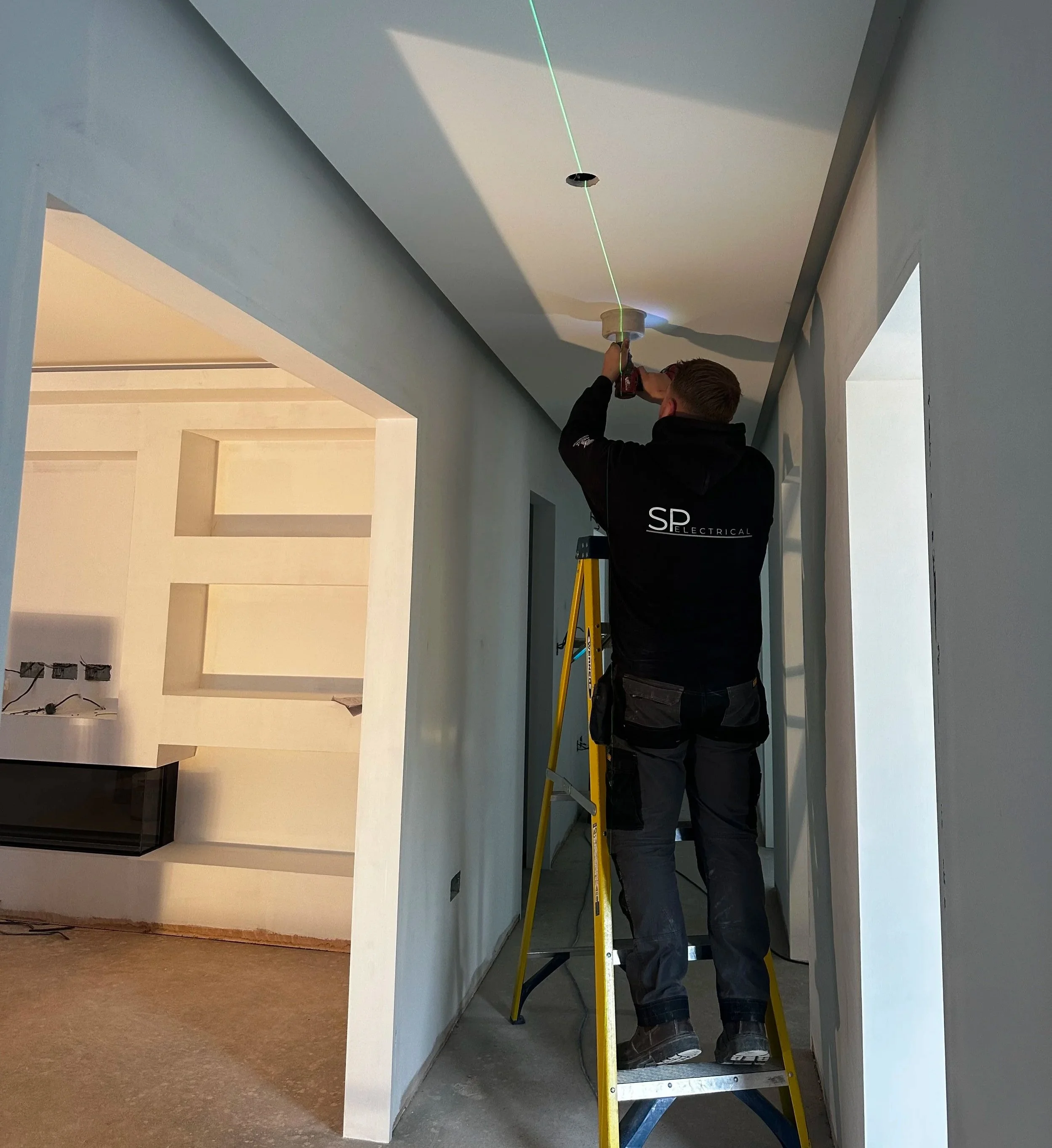 SP Electrical electrician installing ceiling lighting from a ladder inside a renovated home.