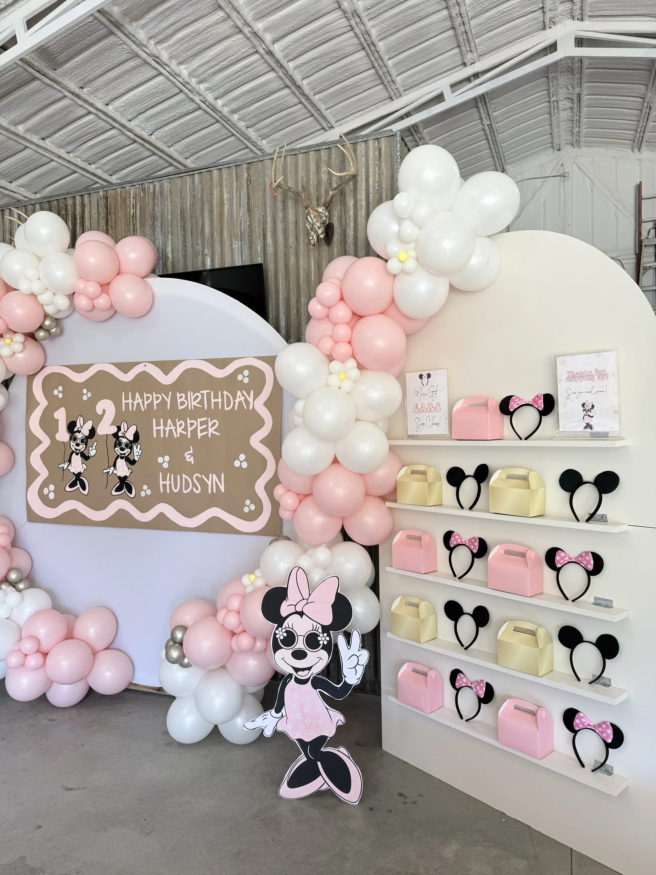 Decorative birthday party setup with pink and white balloons, a cartoon Minnie Mouse cutout, and a sign reading 'Happy Birthday Harper & Hudson.'