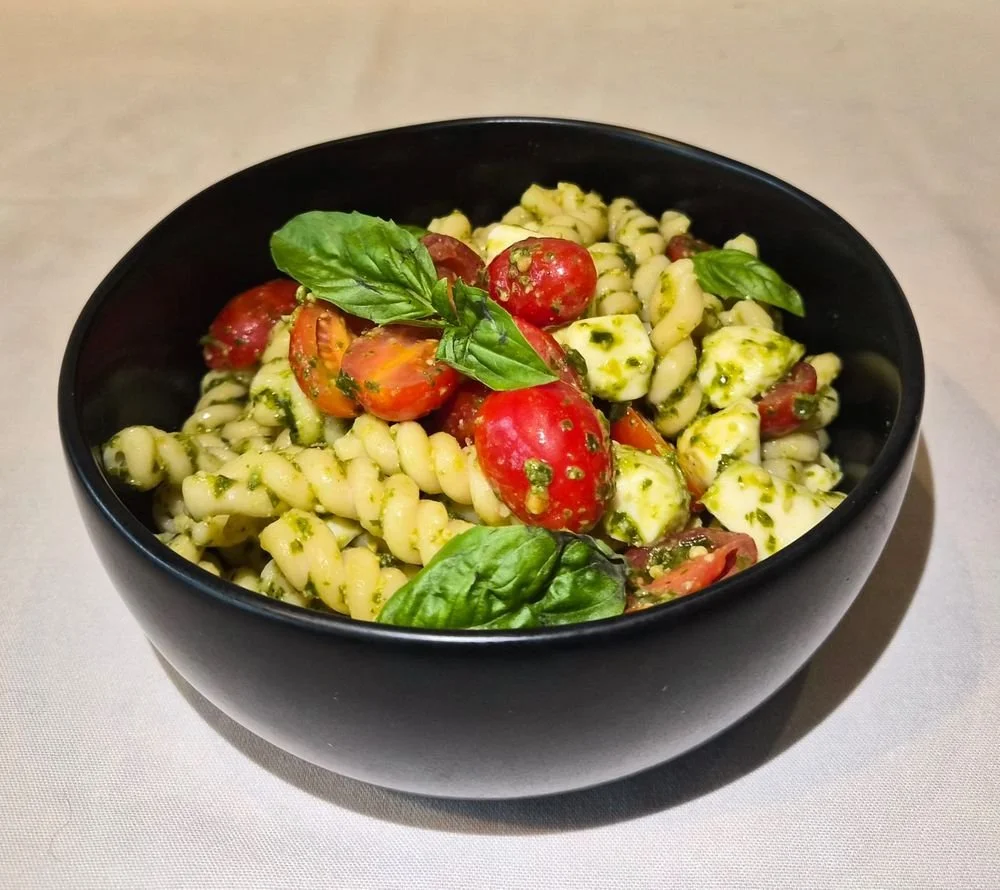 A black bowl of pasta with cherry tomatoes, fresh basil leaves, and pesto sauce.
