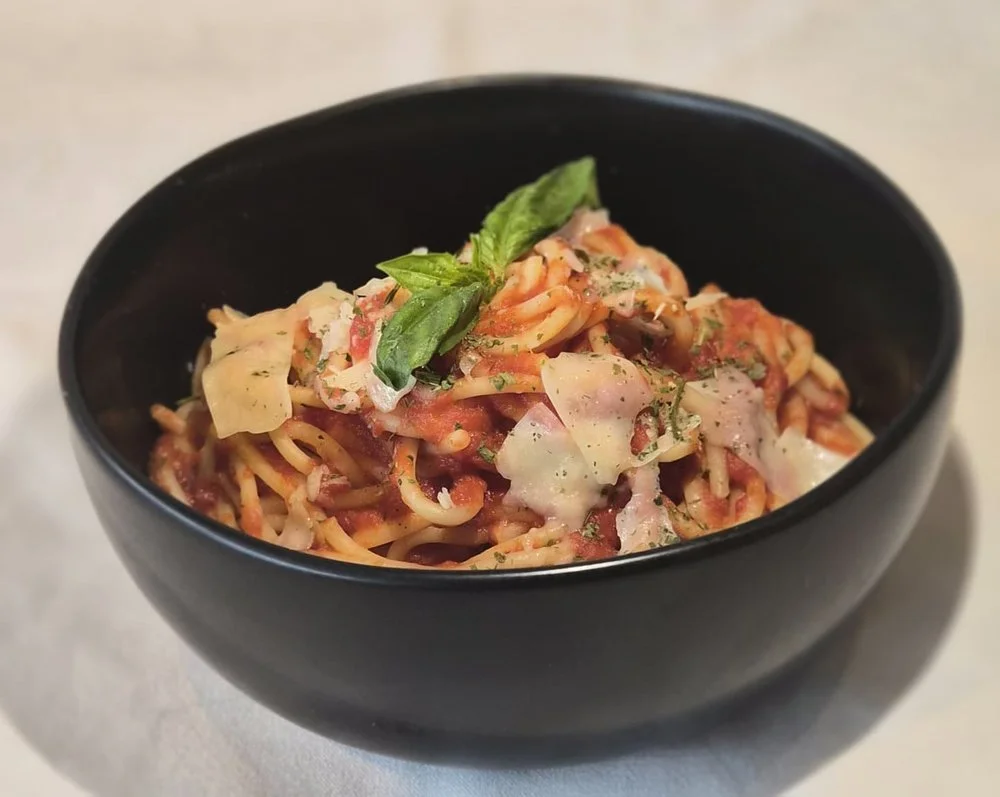 A bowl of pasta topped with basil and grated cheese.