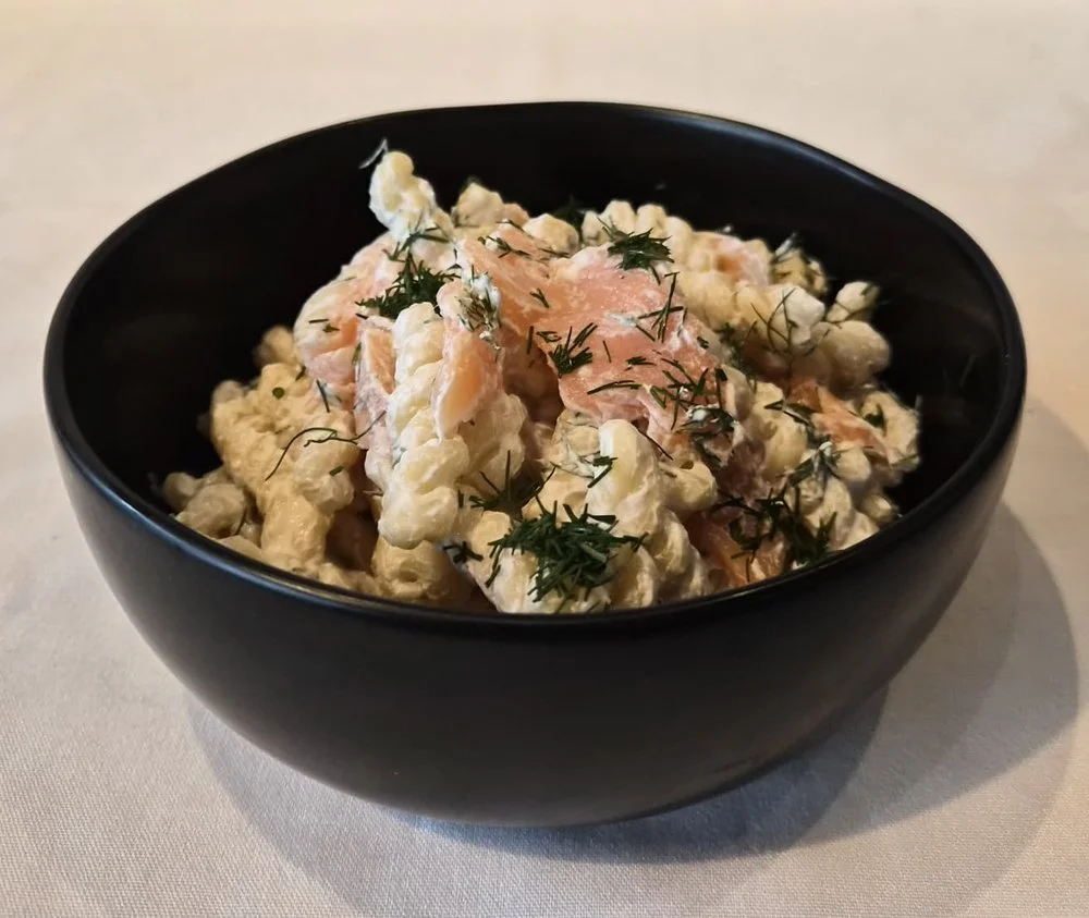A black bowl of potato salad garnished with dill herbs.