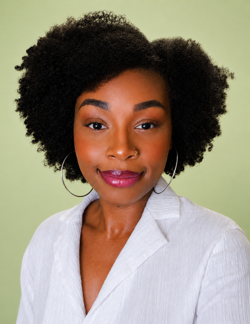Close-up of a woman with curly black hair, wearing hoop earrings and a white blouse, smiling at the camera against a light green background.
