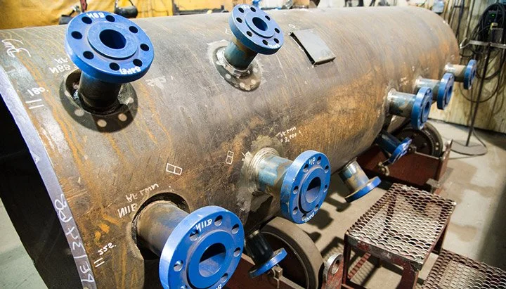 Close-up of welded nozzles with blue flanges on a steel pressure vessel in fabrication