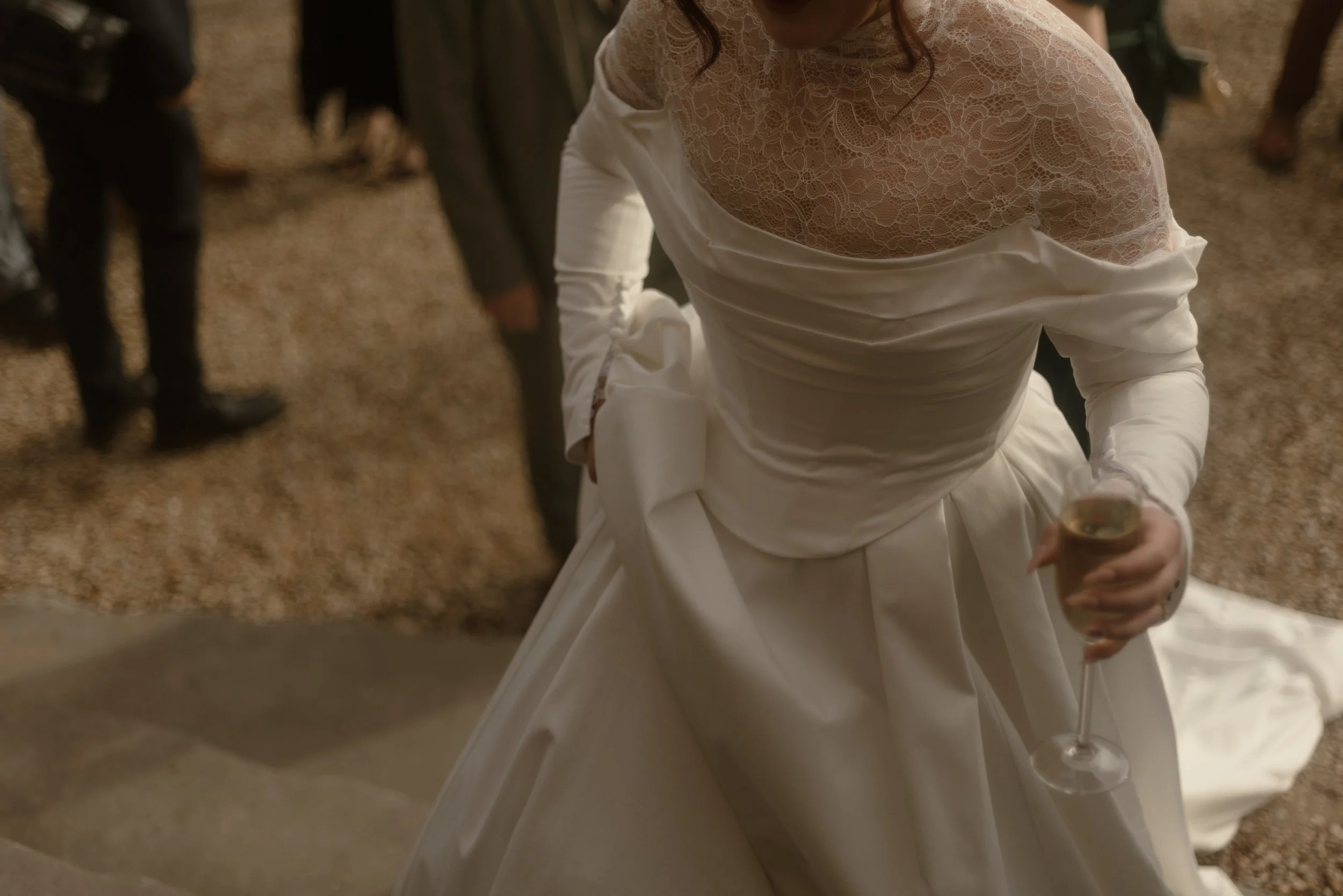 A bride in a white lace dress holding a glass of champagne at a wedding reception.