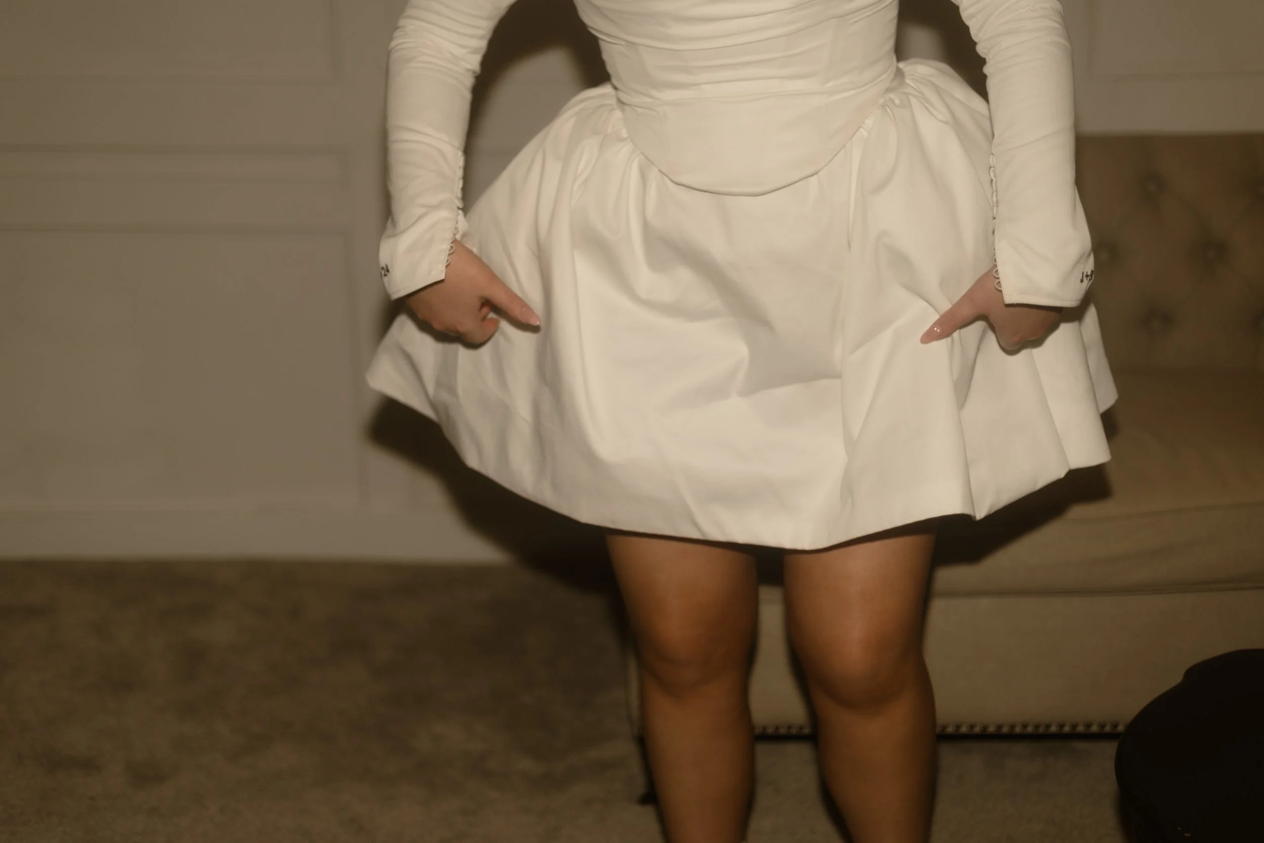 A person wearing a vintage wedding dress with long sleeves, a fitted bodice, and a full skirt, standing indoors.