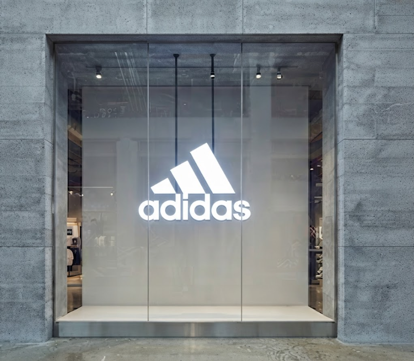 Minimalist storefront window showcasing a clean, illuminated Adidas logo against neutral architectural finishes.