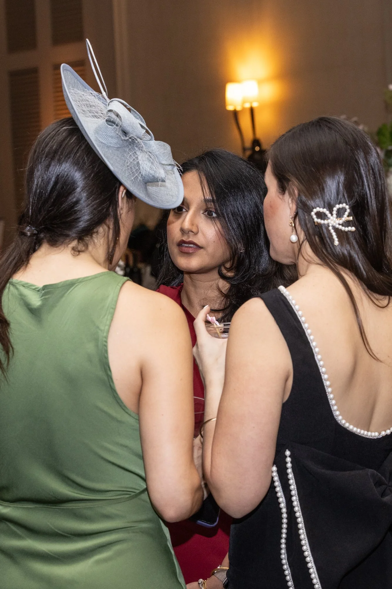 Three women face each other closely in conversation at an indoor social event, with a warm lighting background.
