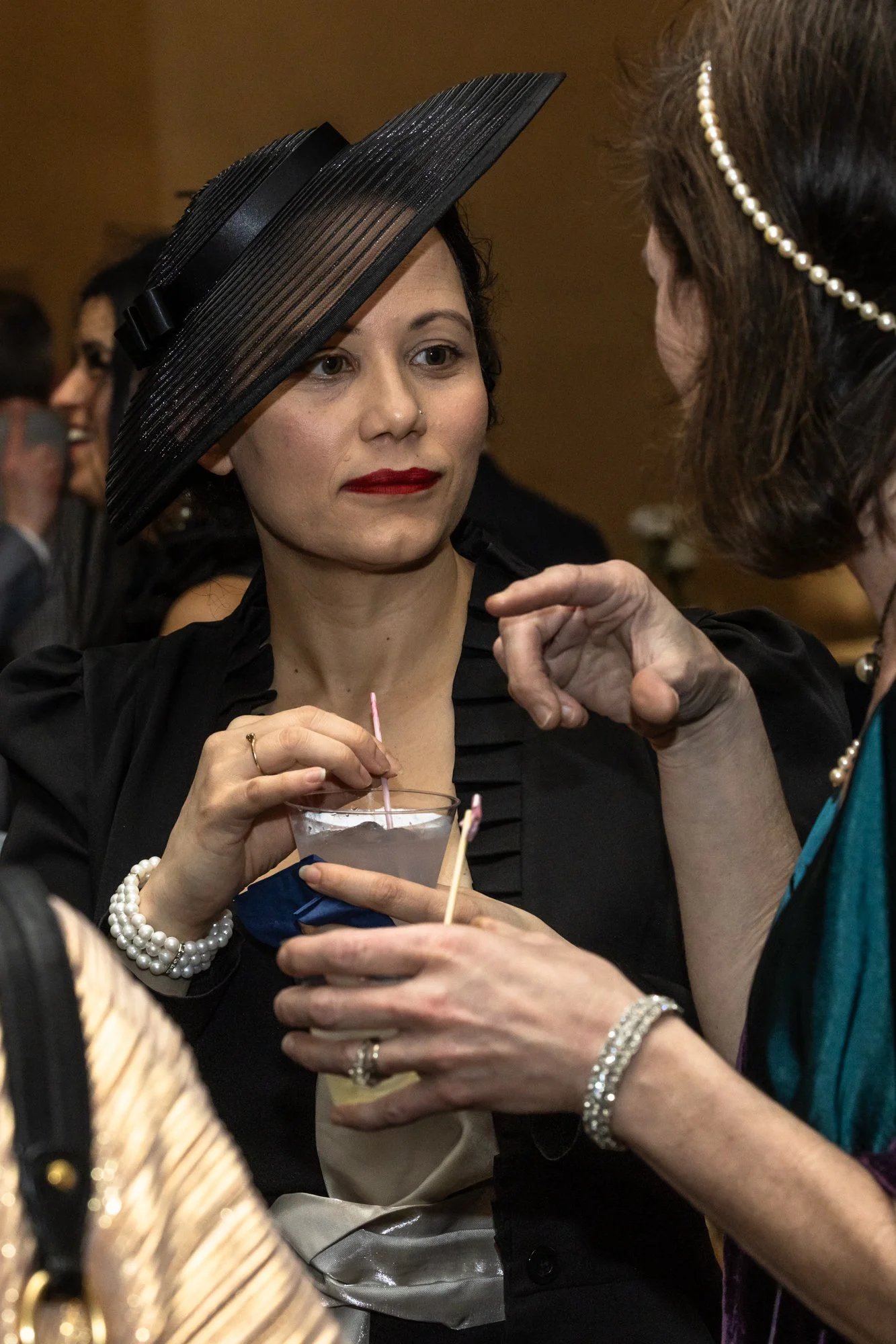 Women at a social gathering wearing elegant attire and pearl jewelry, holding a cocktail with a pink straw