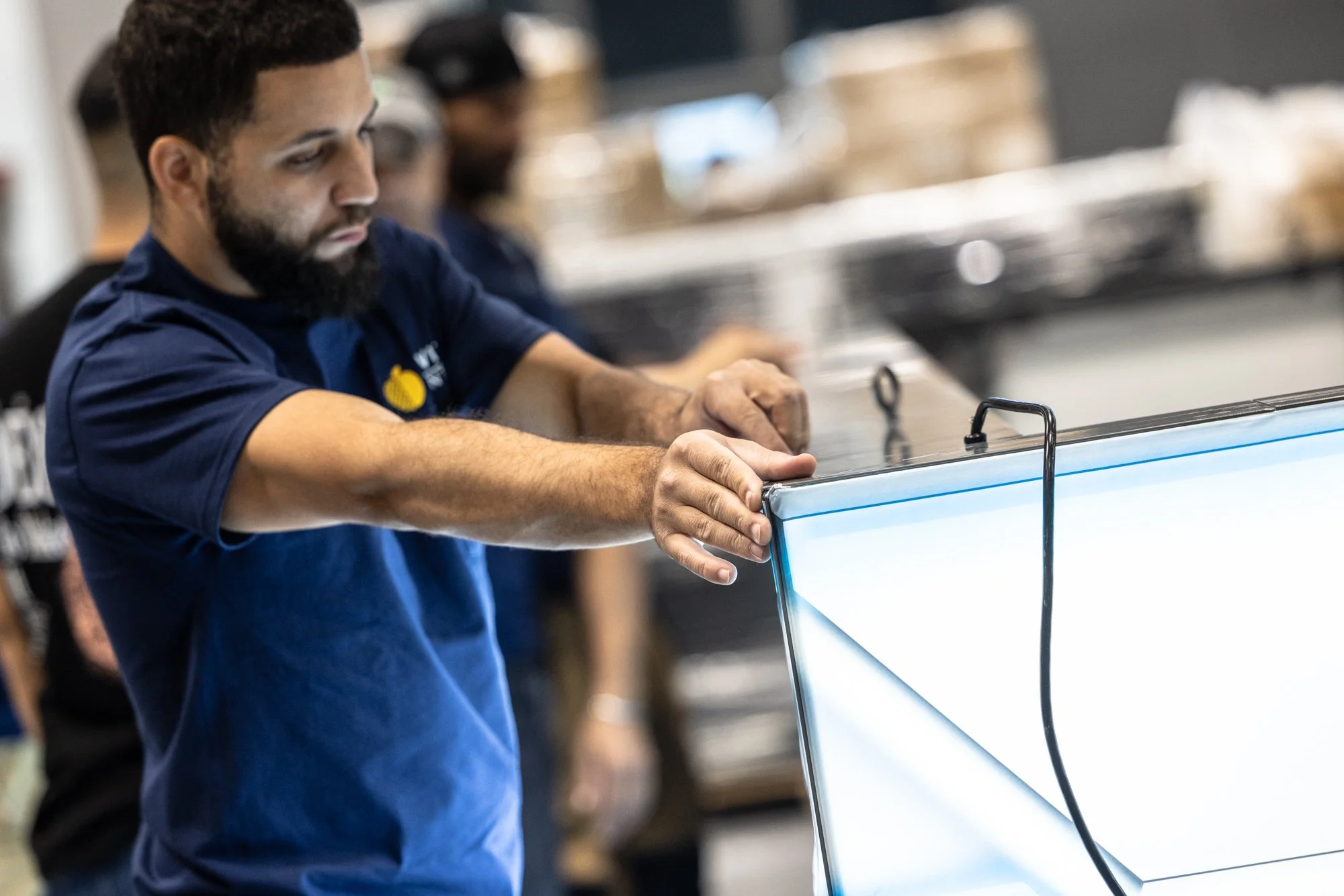 Bearded retail employee in a navy shirt arranging a glass display case in a store