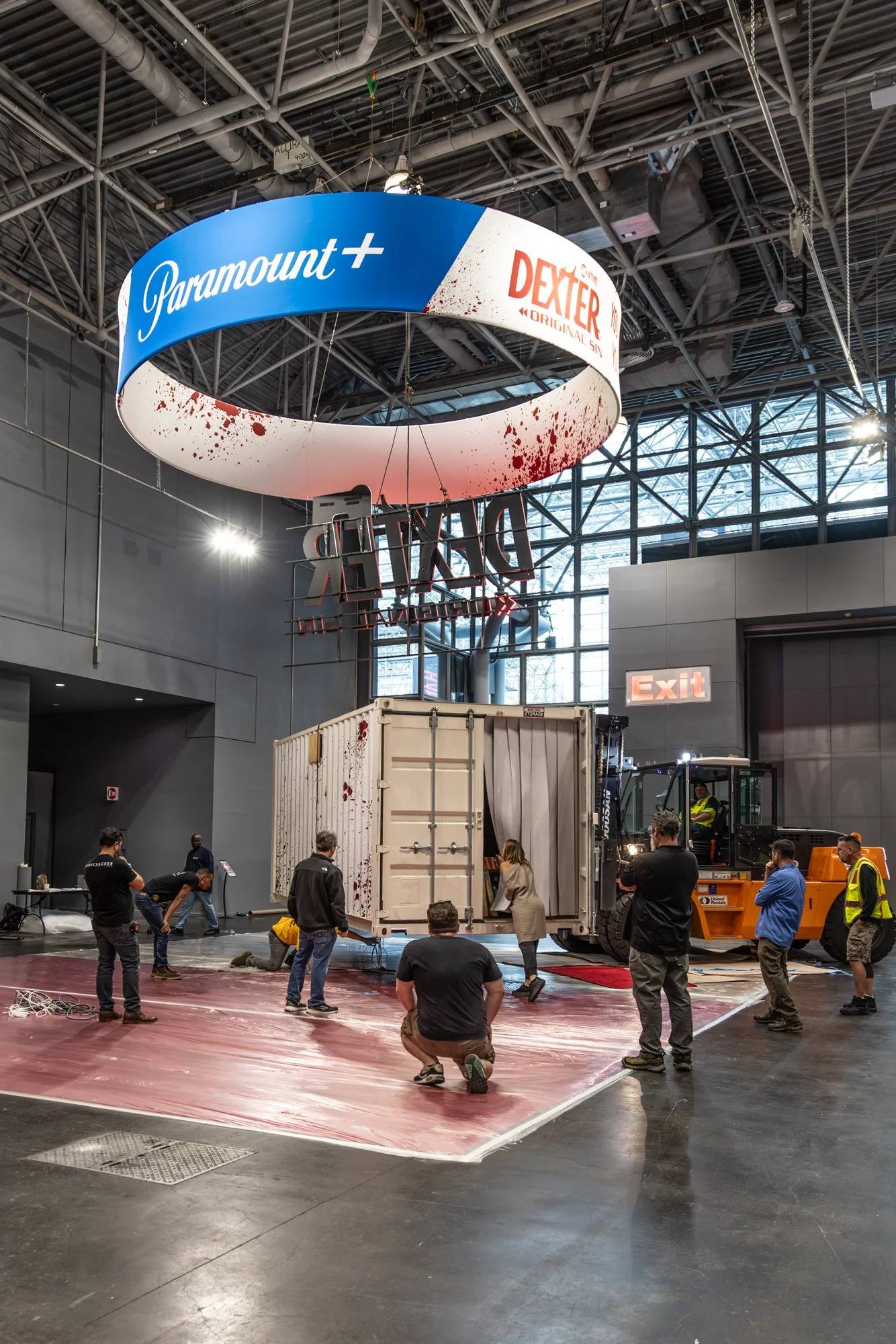 Workers install a blood-splattered Paramount+ and Dexter: Original Sin promotional display inside an industrial venue.