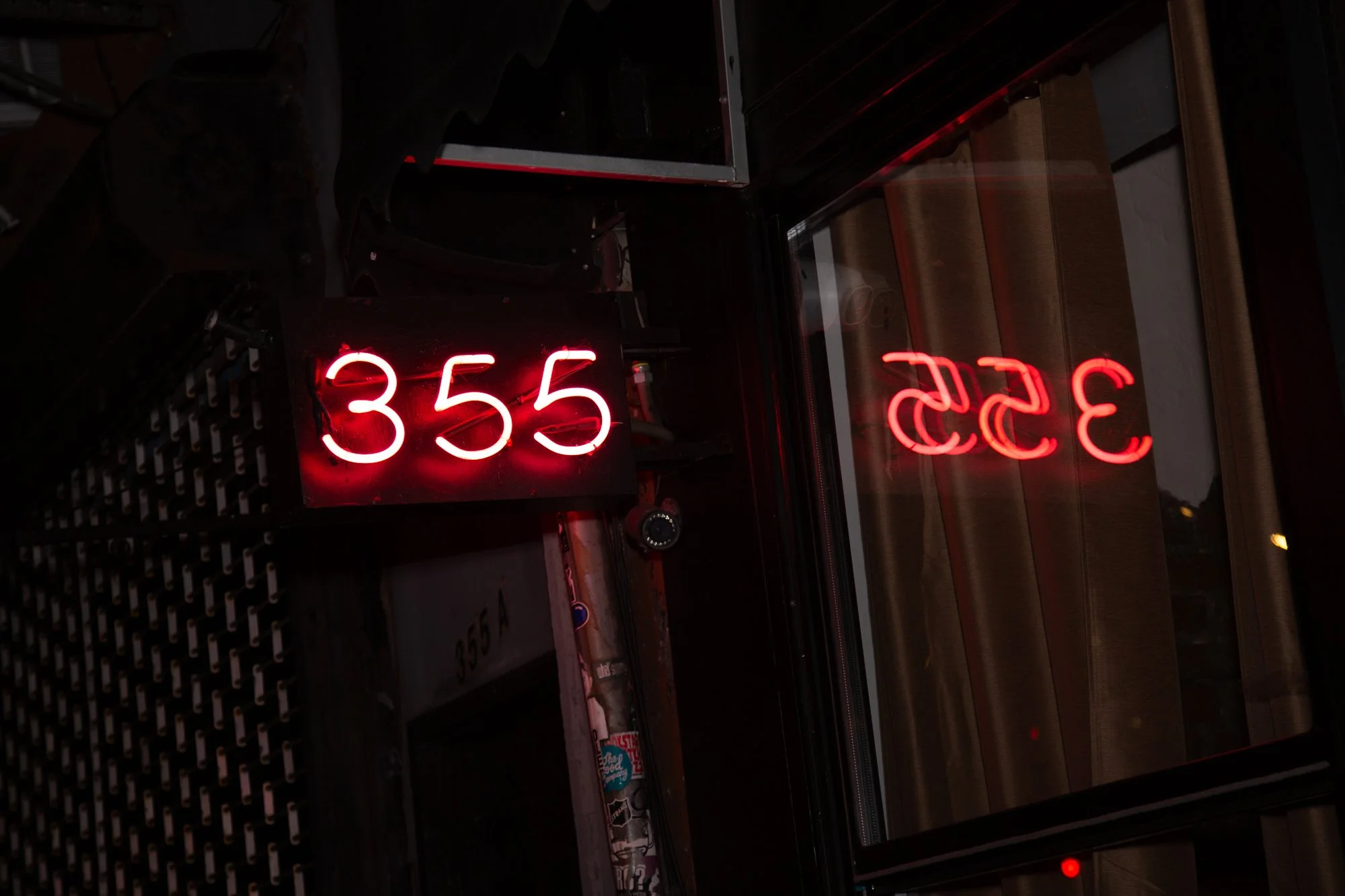 A red digital clock displaying the time 3:55, placed on a black surface, with reflections of the same numbers in the glass behind.