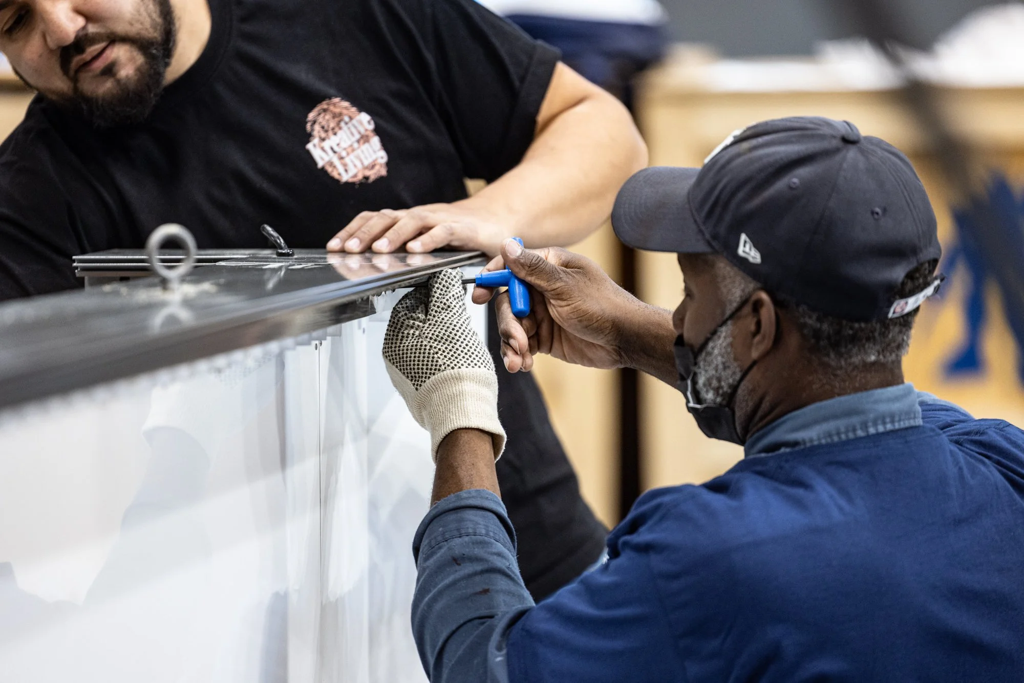 Two workers measure and mark a large metal appliance or panel during installation.