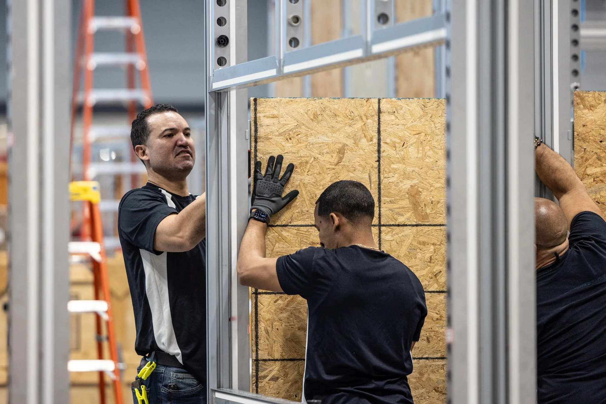 Construction workers installing an OSB sheathing panel inside a metal-framed building