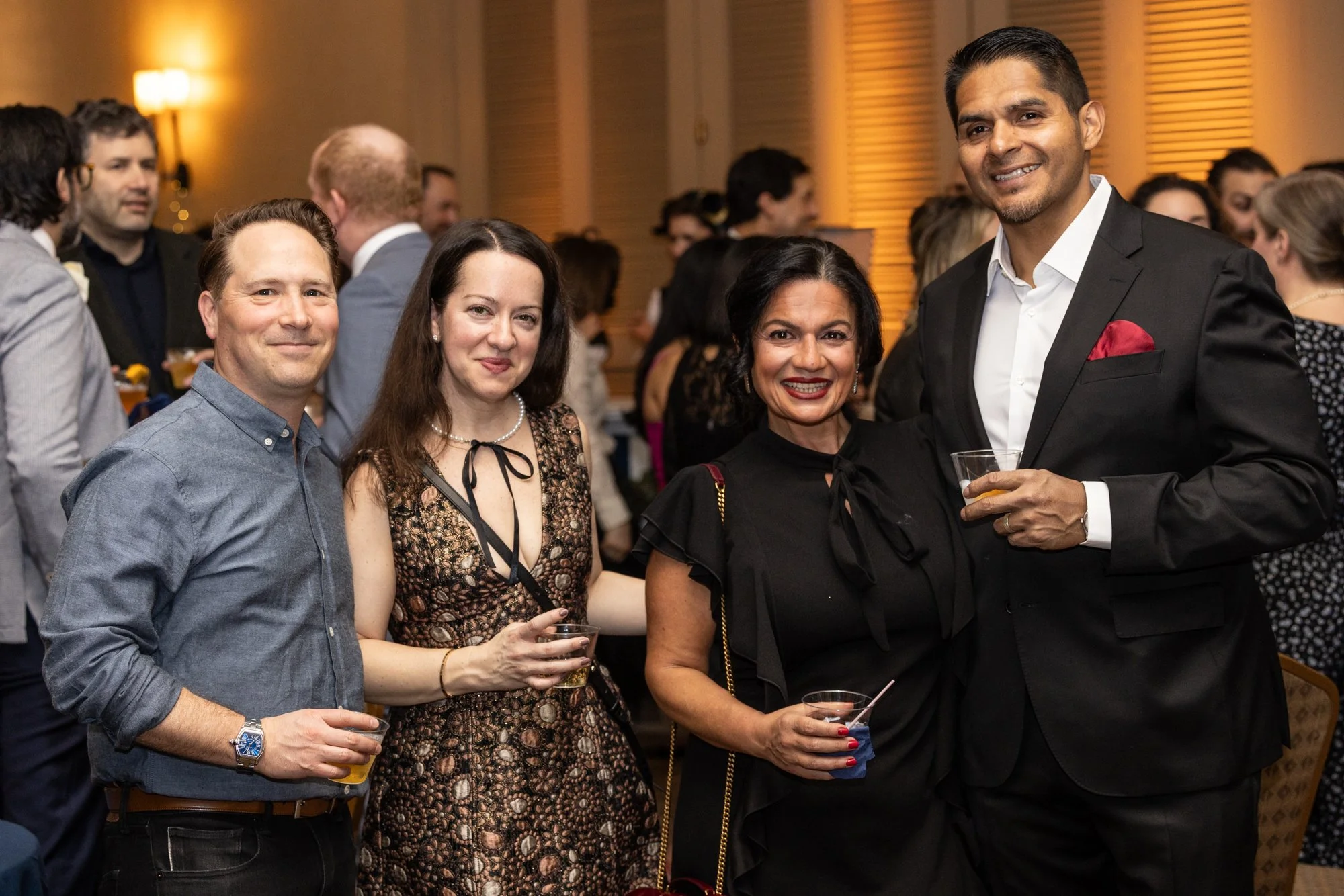 Group of five people smiling and holding drinks at a formal event or party in a warmly lit room with wood paneling.