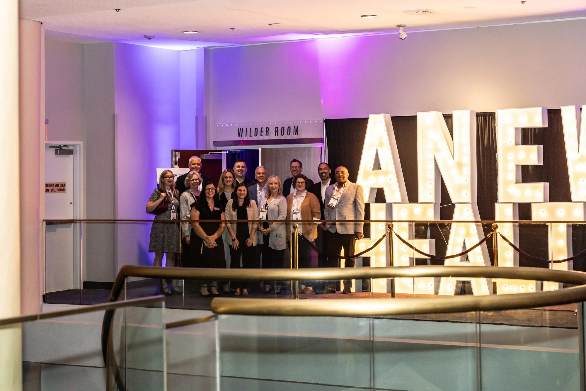 Group of people standing together in front of illuminated 'LOVE' sign at event, with purple and warm lighting, inside conference or hotel lobby area.